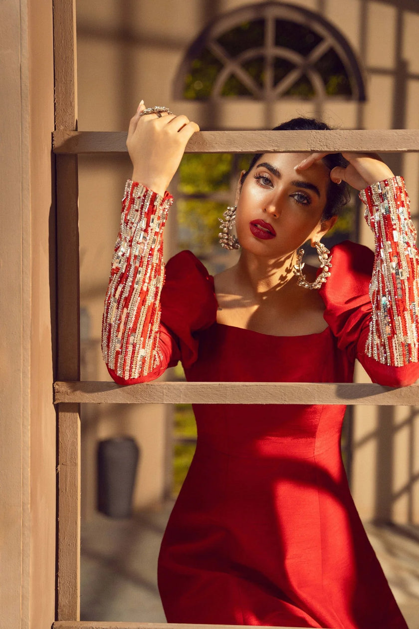 Woman in a red dress with decorative sleeves standing behind a wooden lattice.