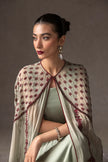 Woman wearing a light-colored embroidered shawl against a neutral background
