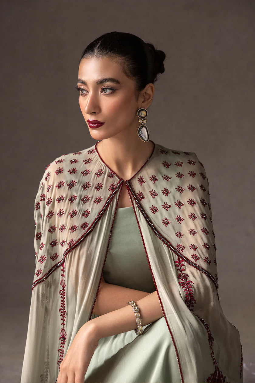 Woman wearing a light-colored embroidered shawl against a neutral background