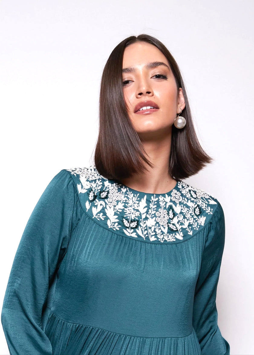 Woman wearing a teal dress with floral embroidery on a white background