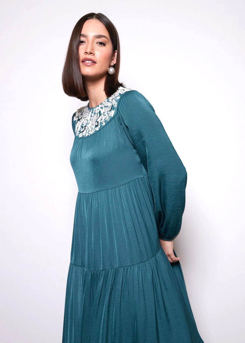 Woman wearing a teal dress with floral embellishments on a white background