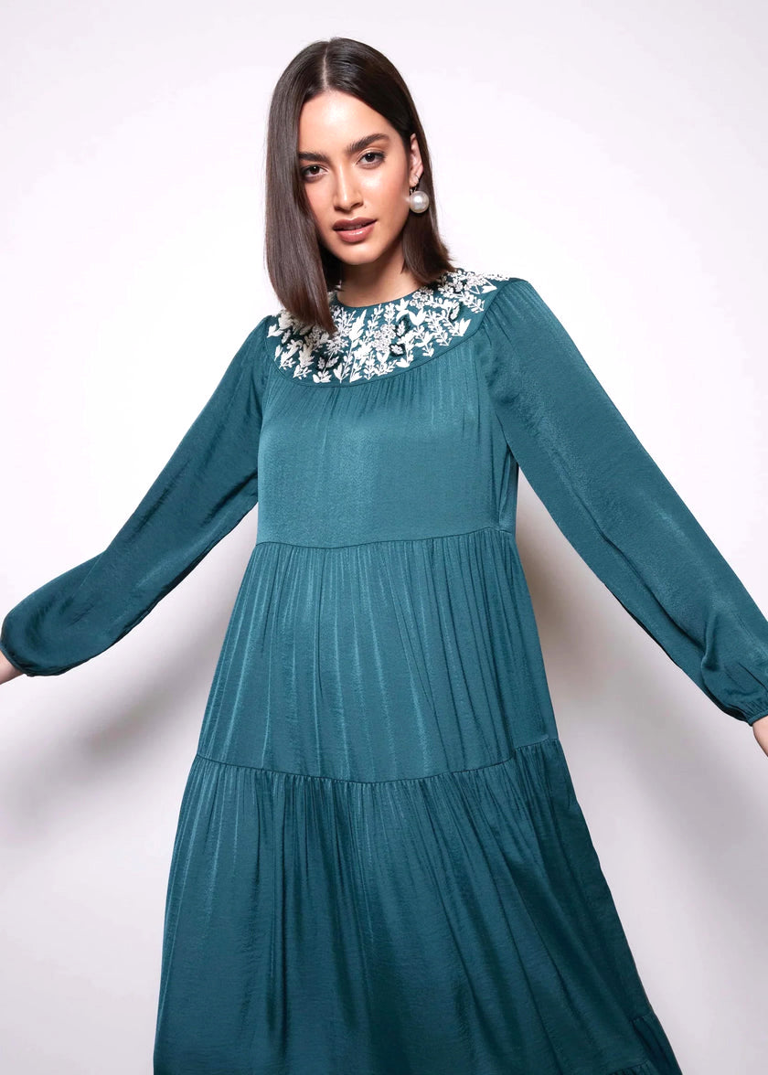 Woman wearing a teal dress with floral embellishments on a white background