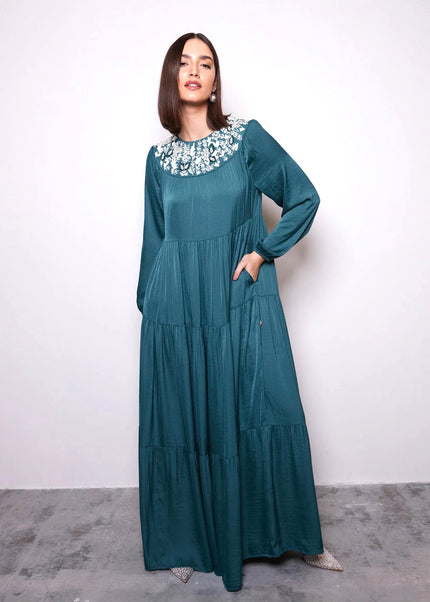 Woman wearing a teal long-sleeve dress with a white floral collar against a white background