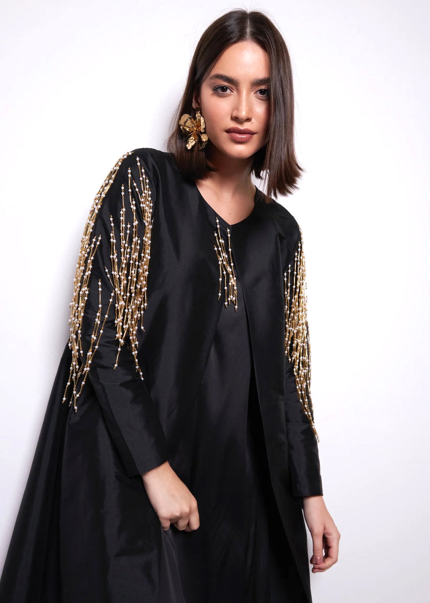 Woman wearing a black outfit with gold embellishments on sleeves against a white background