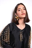 Woman wearing a black outfit with gold embellishments and gold earrings against a white background