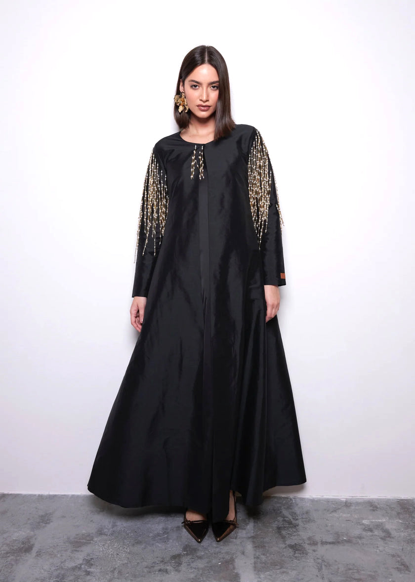 Woman wearing a black dress with gold embroidery on sleeves against a white background