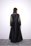 Black evening gown with gold embellishments on sleeves against a white background