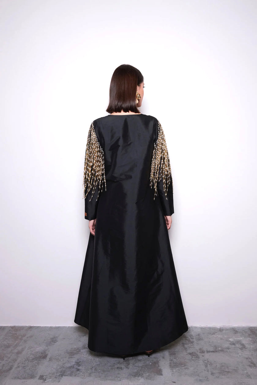 Black evening gown with gold embellishments on sleeves against a white background