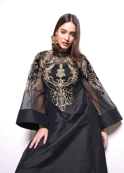 Woman wearing a black dress with gold embroidery on a white background