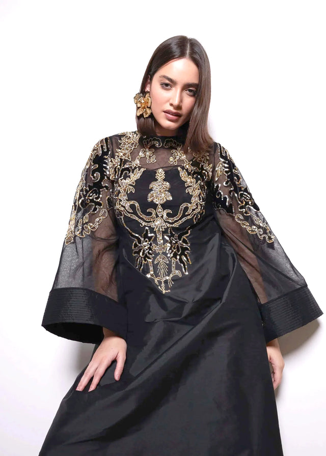Woman wearing a black dress with gold embroidery on a white background