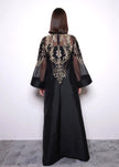 Black dress with gold embroidery worn by a person against a white background
