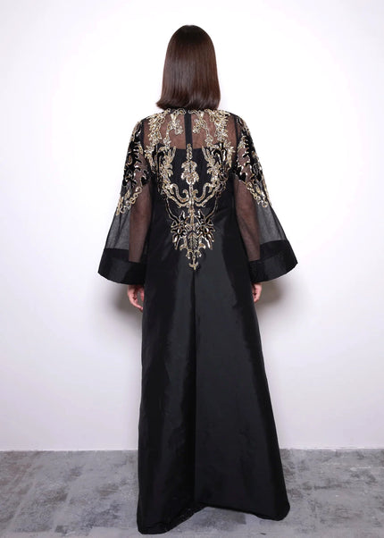 Black dress with gold embroidery worn by a person against a white background