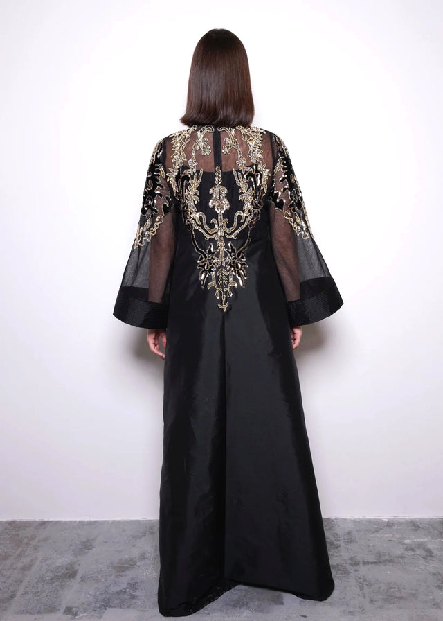 Black dress with gold embroidery worn by a person against a white background