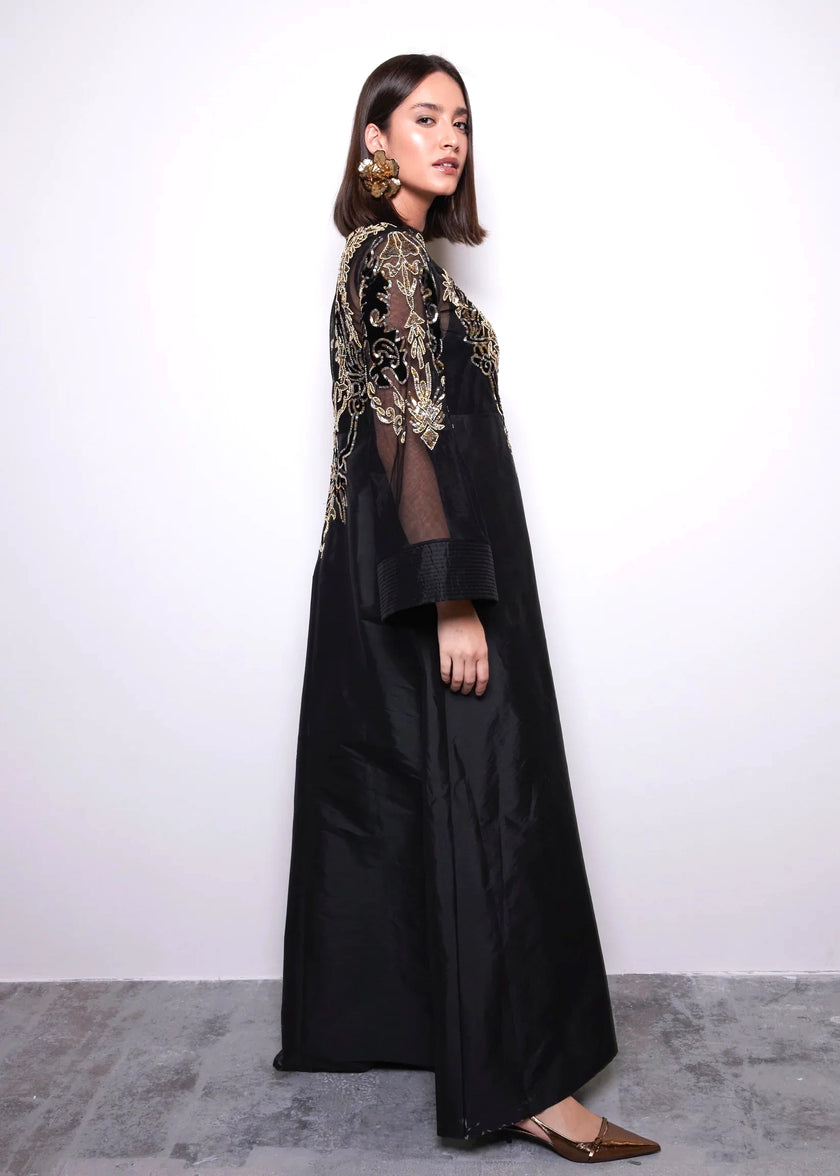 Woman wearing a black dress with gold embroidery against a white background