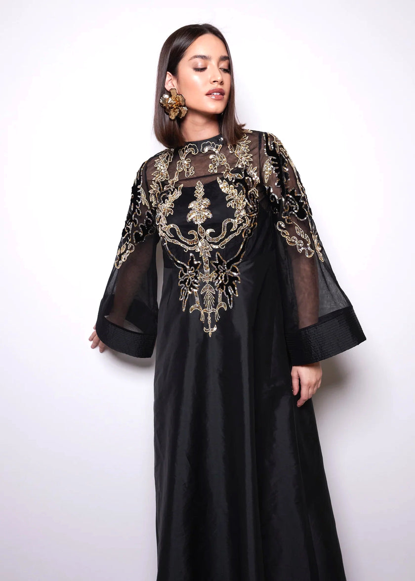 Woman wearing a black dress with gold embroidery on a white background