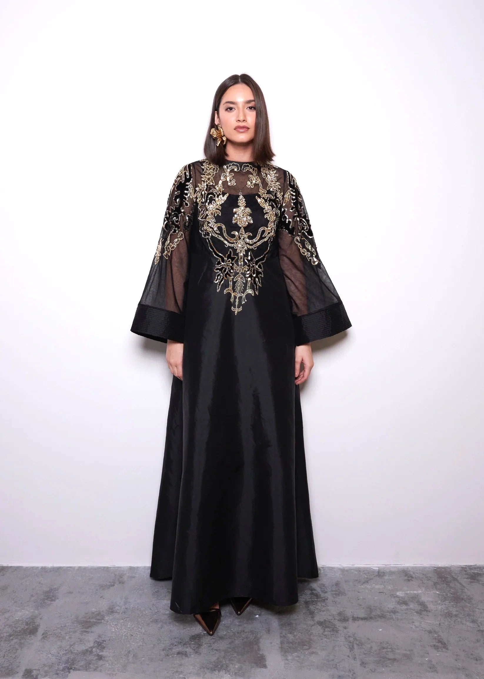 Woman wearing a black dress with gold embroidery against a white background
