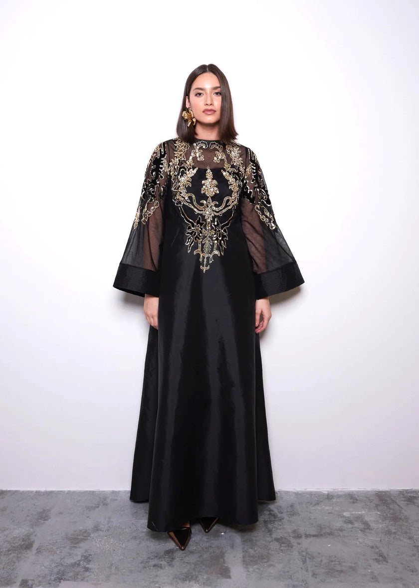 Woman wearing a black dress with gold embroidery against a white background