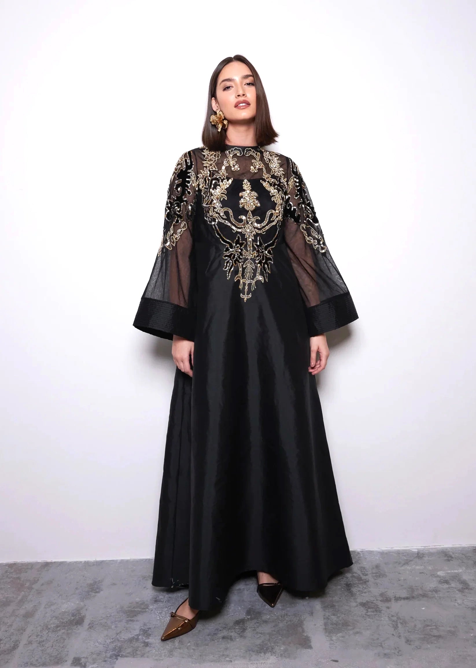 Woman wearing a black dress with gold embroidery against a white background