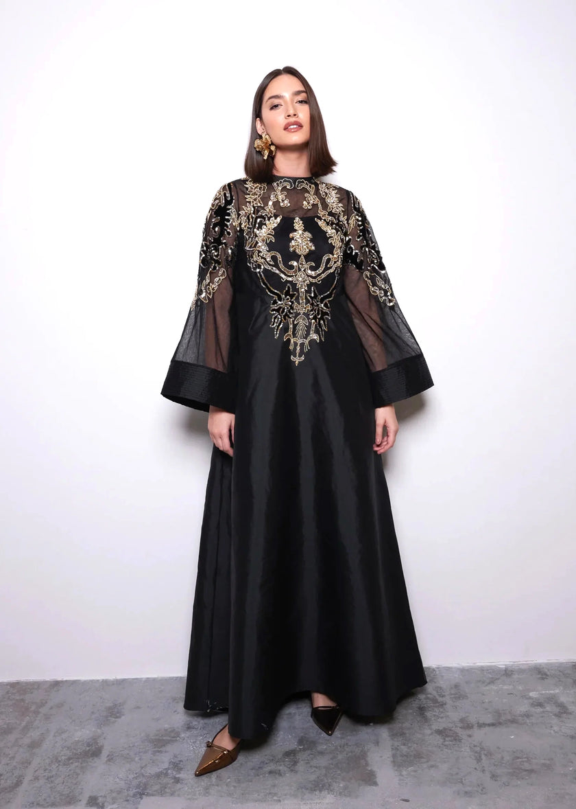 Woman wearing a black dress with gold embroidery against a white background