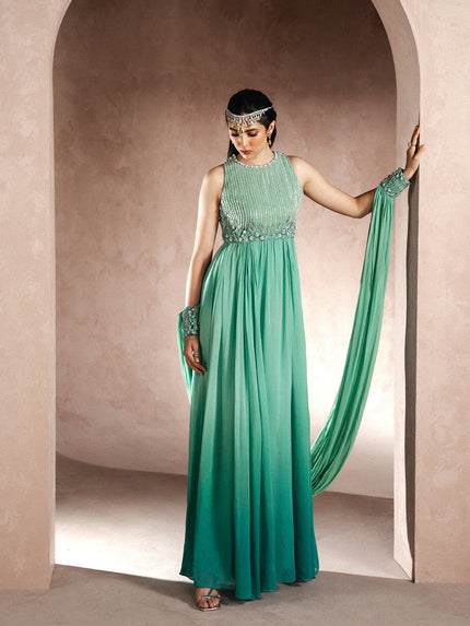 Woman in a green evening gown with a headband and gloves standing in an archway.