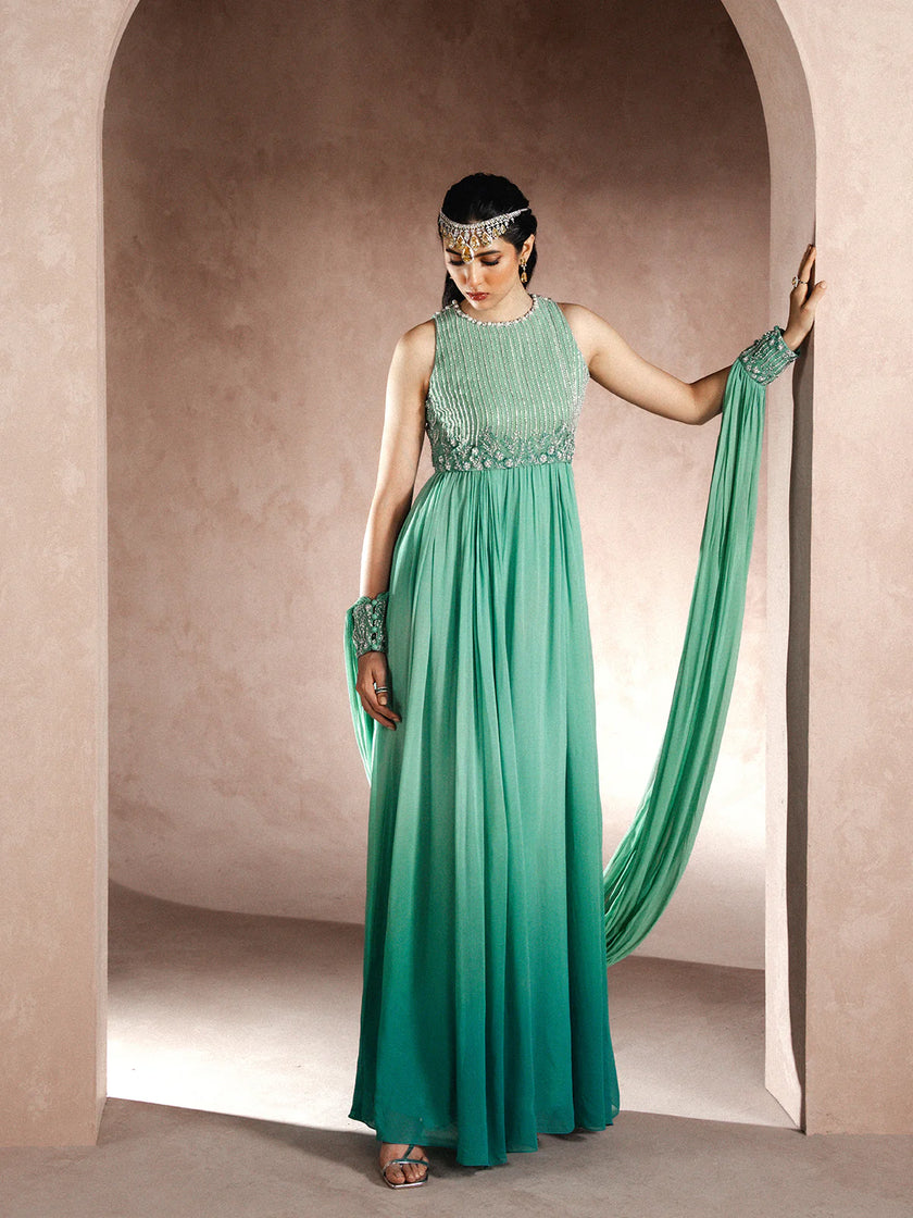 Woman in a green evening gown with a headband and gloves standing in an archway.